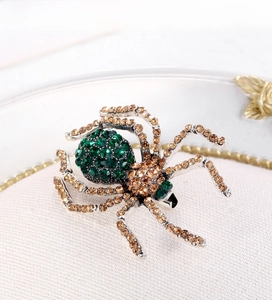 Detailed close-up of a spider brooch with green and amber rhinestones in silver alloy
