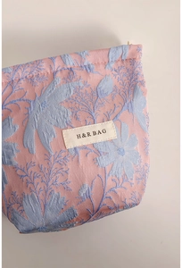 Detail of pink fabric makeup bag featuring blue jacquard floral patterns and H&R logo