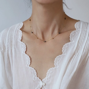 Dettaglio di perline blu stellate e grani dorati su una collana delicata indossata da una modella