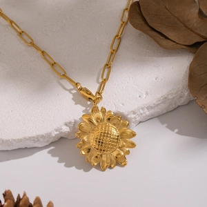 Golden sunflower pendant necklace with paperclip chain on a rustic textured stone surface