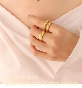 Detail shot of a hand wearing two gold-plated rings with quilted and textured patterns