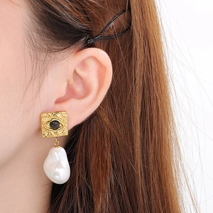 Close-up of a gold eye motif stud with a dangling baroque pearl on a model's ear