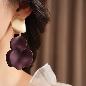 Close-up of golden irregular flower drop earrings with deep purple resin petals on a model