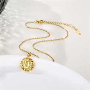 Close-up of gold circle pendant with letter U on a ceramic plate, elegant jewelry detail