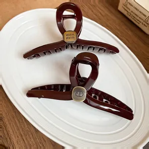 Retro burgundy acrylic hair claws with gold logo plates on a ceramic tray