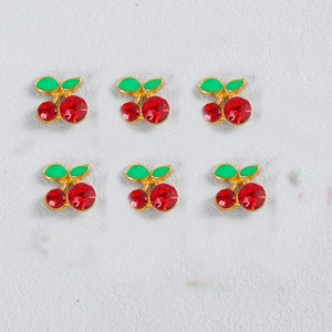 Detailed view of cherry-shaped nail art charms with red rhinestones and green leaves