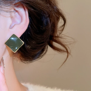 Detail view of model wearing green enamel square earrings with gold-plated geometric borders
