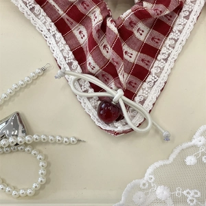 Detailed view of red plaid hair tie featuring white lace edges and a cherry pendant