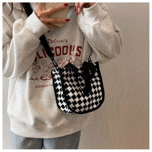 Detailed view of black and white checkered knit handbag with black top handles and soft texture