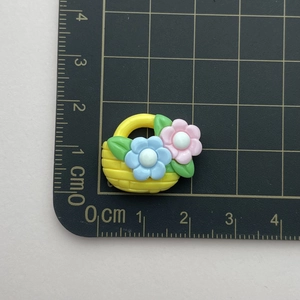Flat lay of a yellow resin flower basket charm on a ruler showing 3cm x 2.5cm dimensions