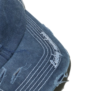 Detail of distressed brim on washed blue denim baseball cap with white embroidery