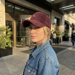 Burgundy herringbone baseball cap with gold crown logo worn outdoors in sunlight