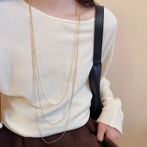Detail view of triple-layered gold tassel necklace with beads on textured sweater