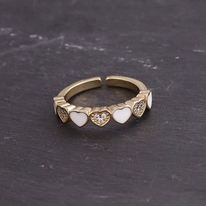 Close-up of gold-plated heart ring with white enamel and micro-pave zircons on black stone