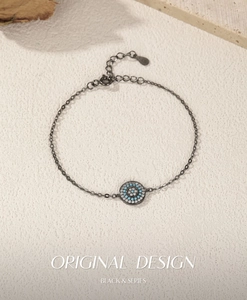 Détail d'un bracelet chaîne noire avec pendentif œil protecteur et zircons bleu et blanc