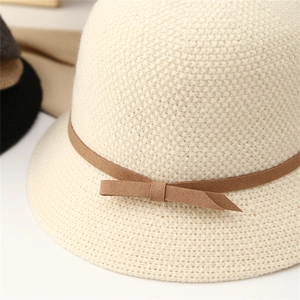 Detail of beige knitted bucket hat featuring a brown suede ribbon and bow decoration