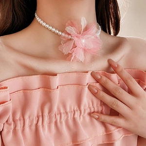 Detail of white pearl necklace with large pink fabric flower on model's neck