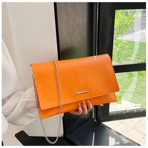 Detailed macro view of orange envelope bag with golden chain and metallic bar detail