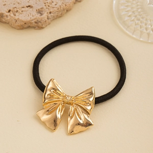 Detail of elegant gold metal bow hair tie with textured ribbon finish on a warm background