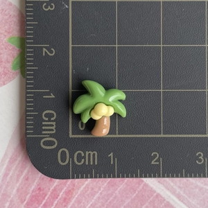 Gros plan d'une mini breloque palmier en résine sur tapis de mesure montrant la taille