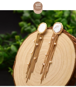 Close-up of baroque pearl tassel earrings with gold chains on a wooden base