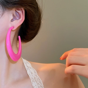 Close-up of model wearing large hot pink C-shaped earrings with a glossy resin finish