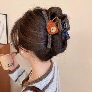 Detailed close-up of a brown knit hair claw clip with orange bow-knot and floral texture