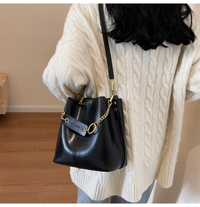 Detail of a black bucket bag with gold chain and strap worn over a white sweater