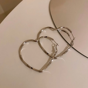 Minimalist silver heart-shaped hoop earrings on white surface with a round mirror
