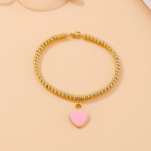 Close-up of 18k gold-plated beaded bracelet with a sweet pink heart charm
