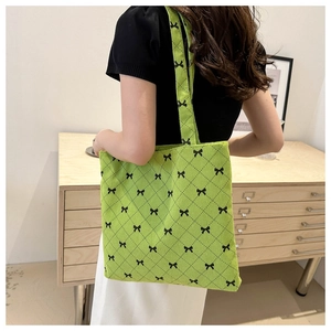 Detail of green corduroy tote bag with black bow patterns worn by a model