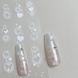 Macro detail of white butterfly and star nail decals on pearl finish press-on nails
