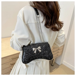 Detail of black sequined crossbody bag with silver metal bow and chain strap on model