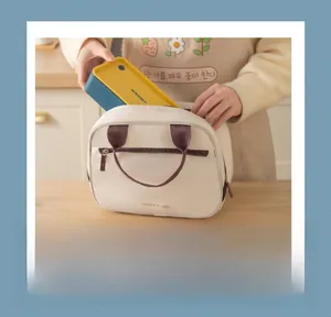 Close-up of a person placing a yellow lunch box into a cream-colored insulated lunch bag