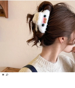 Detail shot of a cute white plush monster hair claw clip worn on a soft knit sweater