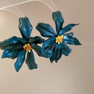 Macro detail of acrylic floral earrings with dark teal petals and amber beaded centers