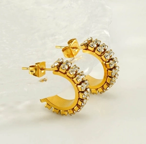 Detailed macro view of double-row rhinestone C-shape gold earrings on ice textured background