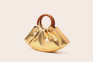 Detail of gold crocodile texture handbag with brown circular hard handle and metallic finish