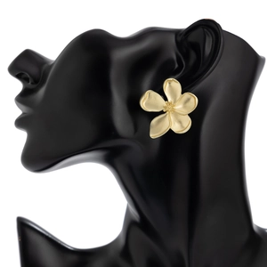 Detailed close-up of matte gold flower earring on a black display stand