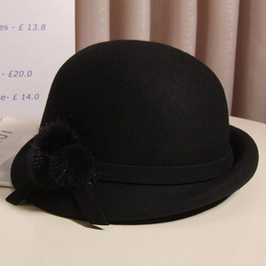 Detail of black wool fedora with plush fur balls and ribbon on a rolled brim