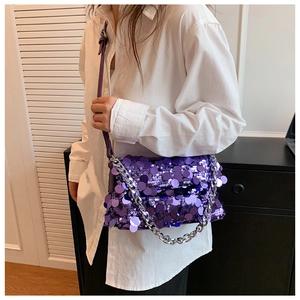 Detail view of purple sequin handbag with silver chain strap worn by a model