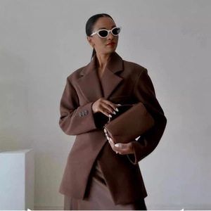 Blazer da donna marrone scuro con borsa in pelle in un ambiente da studio minimalista