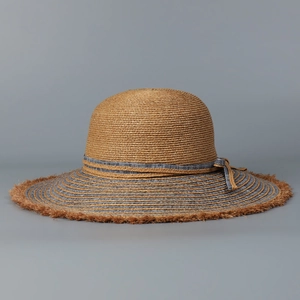 Detailed close-up of wide brim raffia sun hat featuring denim fringe and striped ribbon bow
