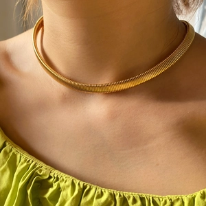 Close-up of a gold ribbed choker necklace featuring a sleek metallic serpent-style texture