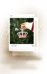 Pink crown-shaped Christmas ornament with intricate hollow details on pine branch