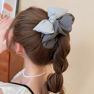Close-up of a large grey plaid fabric bow scrunchie on a model's high ponytail