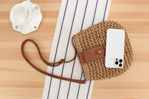 Detail of woven paper straw crossbody bag showing internal capacity compared to a smartphone
