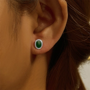 Detail of a green oval opal stud earring with silver edge worn on a female earlobe