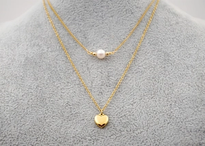 Close-up of double-layer gold necklace with white pearl and heart pendant on model