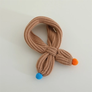 Detail of chunky knit baby scarf with cross-loop closure and colorful pom-poms